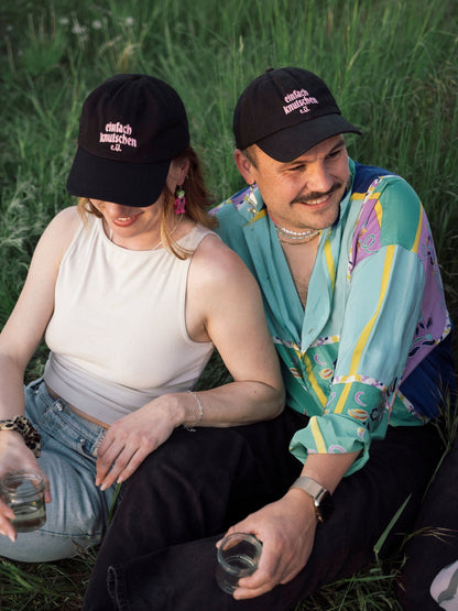 Zwei Personen mit „einfach knutschen e.V.“ Caps sitzen im Gras und genießen den Moment.