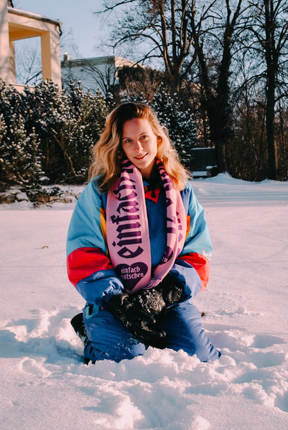 Einfach Knutschen Fanschal in risa mit lila Schriftzug, getragen von einer Person im Schnee – Winter-Fanschals mit auffälligem Branding von einfach knutschen.